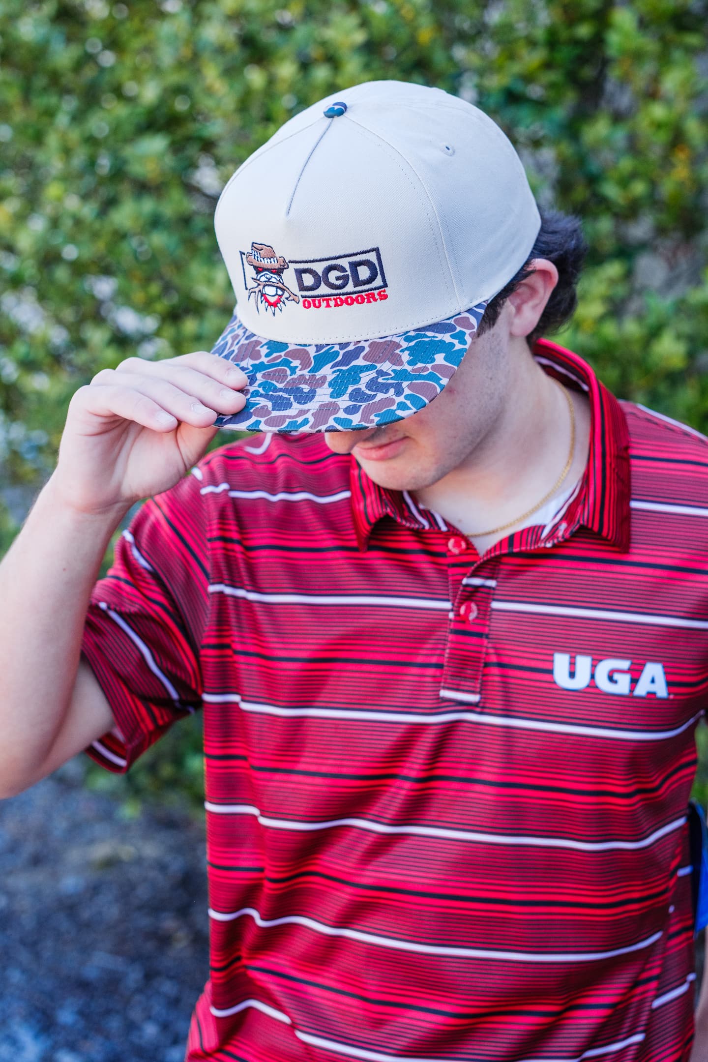 Man wearing a red Georgia Bulldogs gameday polo shirt and a DGD Outdoors leather patch trucker hat with camo brim, available at Anderson’s General Store