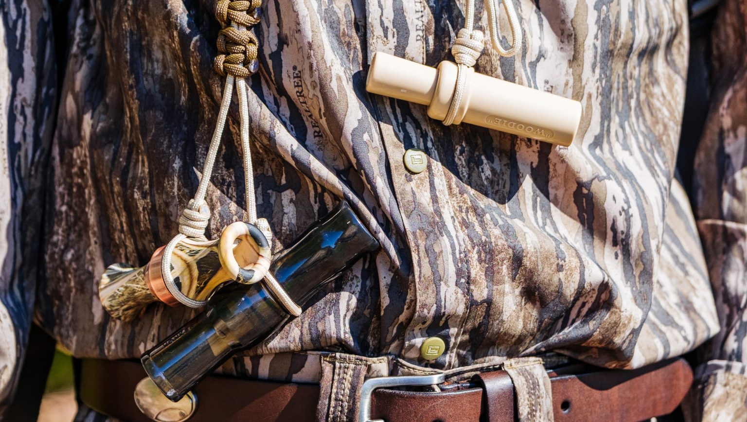 Alt text: “Close-up of a hunter wearing camouflage gear and lanyards with duck calls, featuring Mossy Oak Bottomland apparel available at Anderson’s General Store in Statesboro, Georgia.