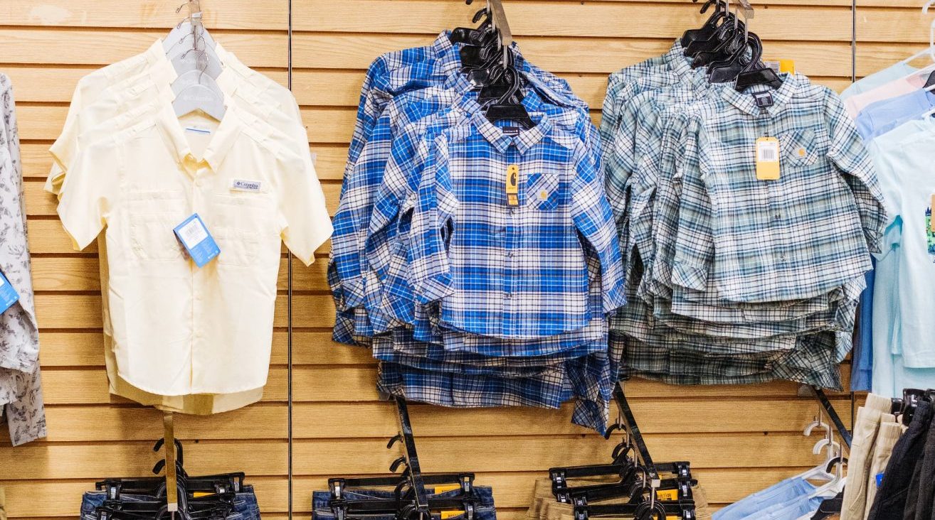 Display of boys’ clothing at Anderson’s General Store featuring plaid button-up shirts, khaki shorts, and denim jeans neatly arranged on hangers against a wooden wall.