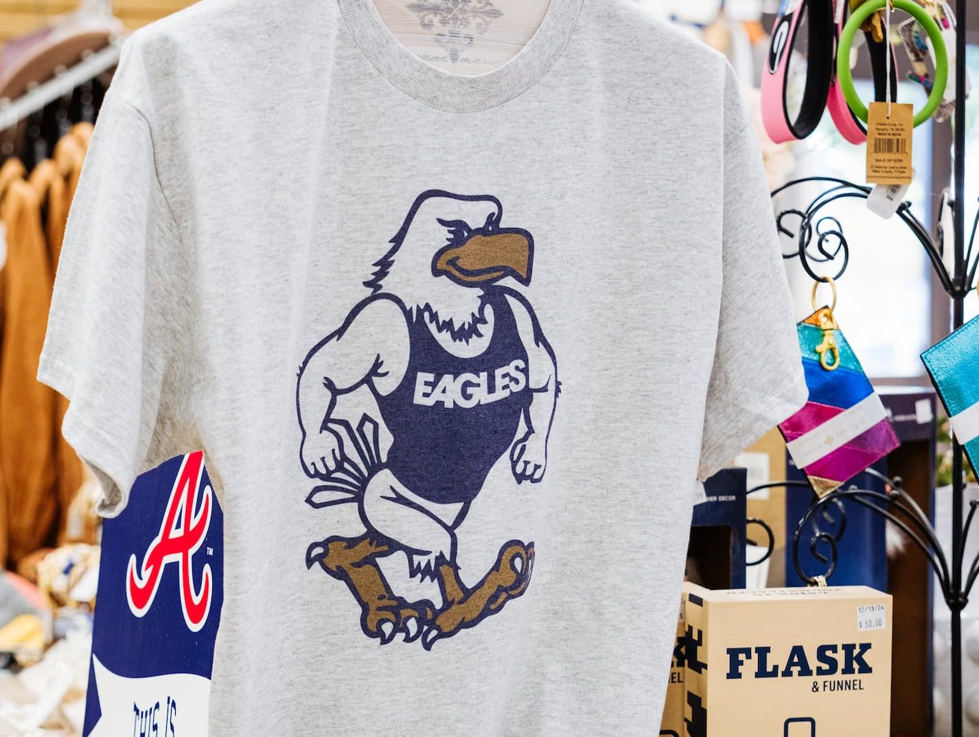 Display table at Anderson’s General Store featuring a gray Georgia Southern Eagles T-shirt, white and navy Anderson’s hats, a Braves sign, and gift items like flasks and keychains.