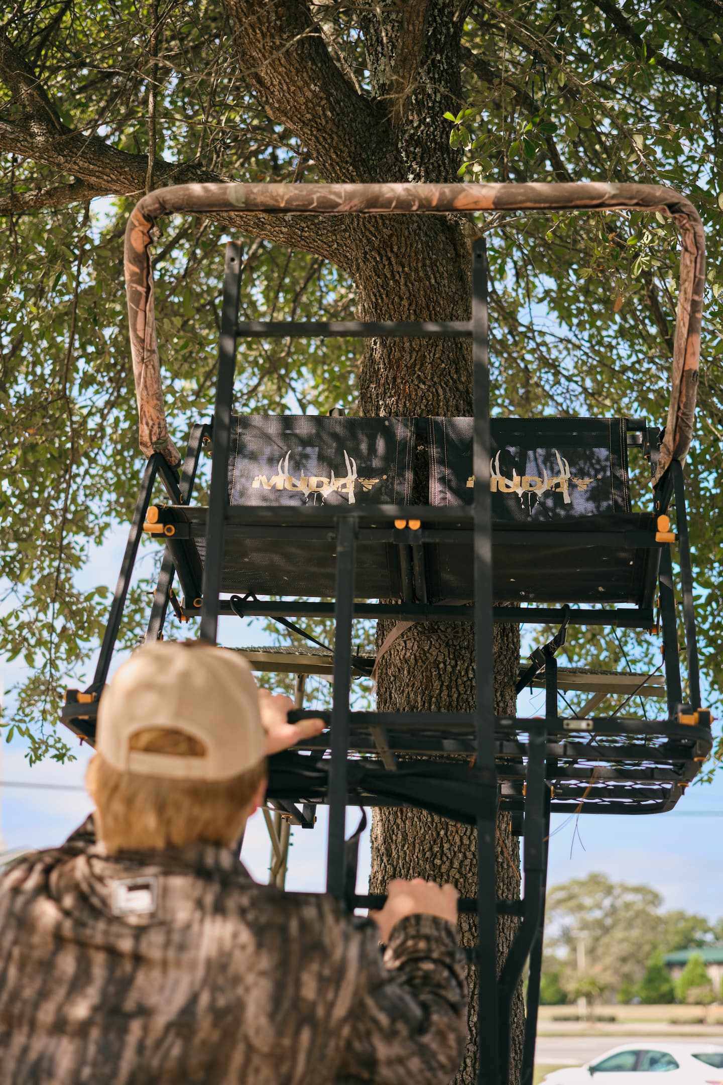 Hunter wearing camouflage climbs a ladder stand attached to a tree, preparing for deer hunting season.