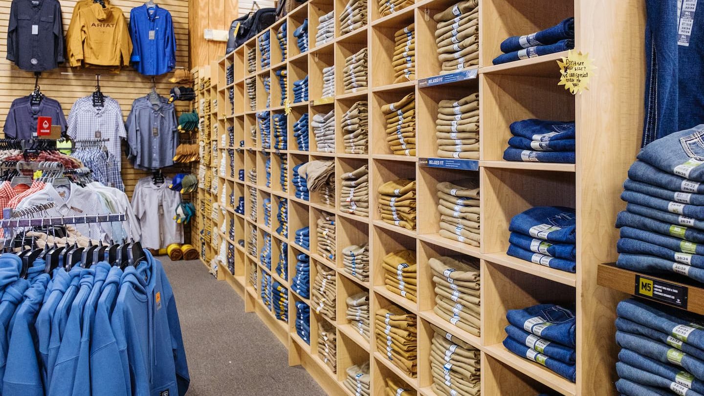 riat jeans and work pants neatly organized on shelves at Anderson’s General Store, surrounded by outerwear and plaid shirts — perfect for durable workwear and hunting apparel in Georgia climates.
