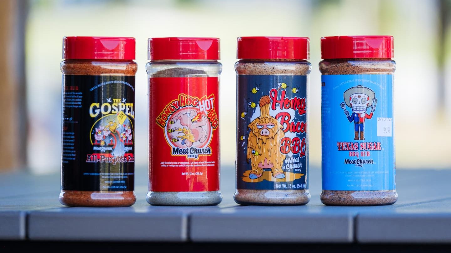 Lineup of Meat Church BBQ seasonings including The Gospel, Honey Hog Hot, Honey Bacon, and Texas Sugar rubs, displayed on a table at Anderson’s General Store.