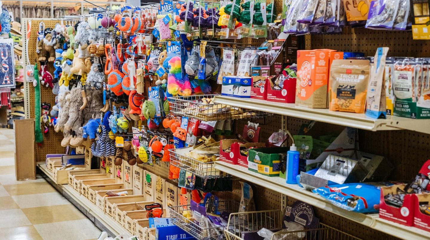 Aisle of pet supplies at Anderson’s General Store featuring colorful dog toys, chews, and treats neatly organized on shelves, including brands like Bark, Tricky Trainers, and No-Hide.