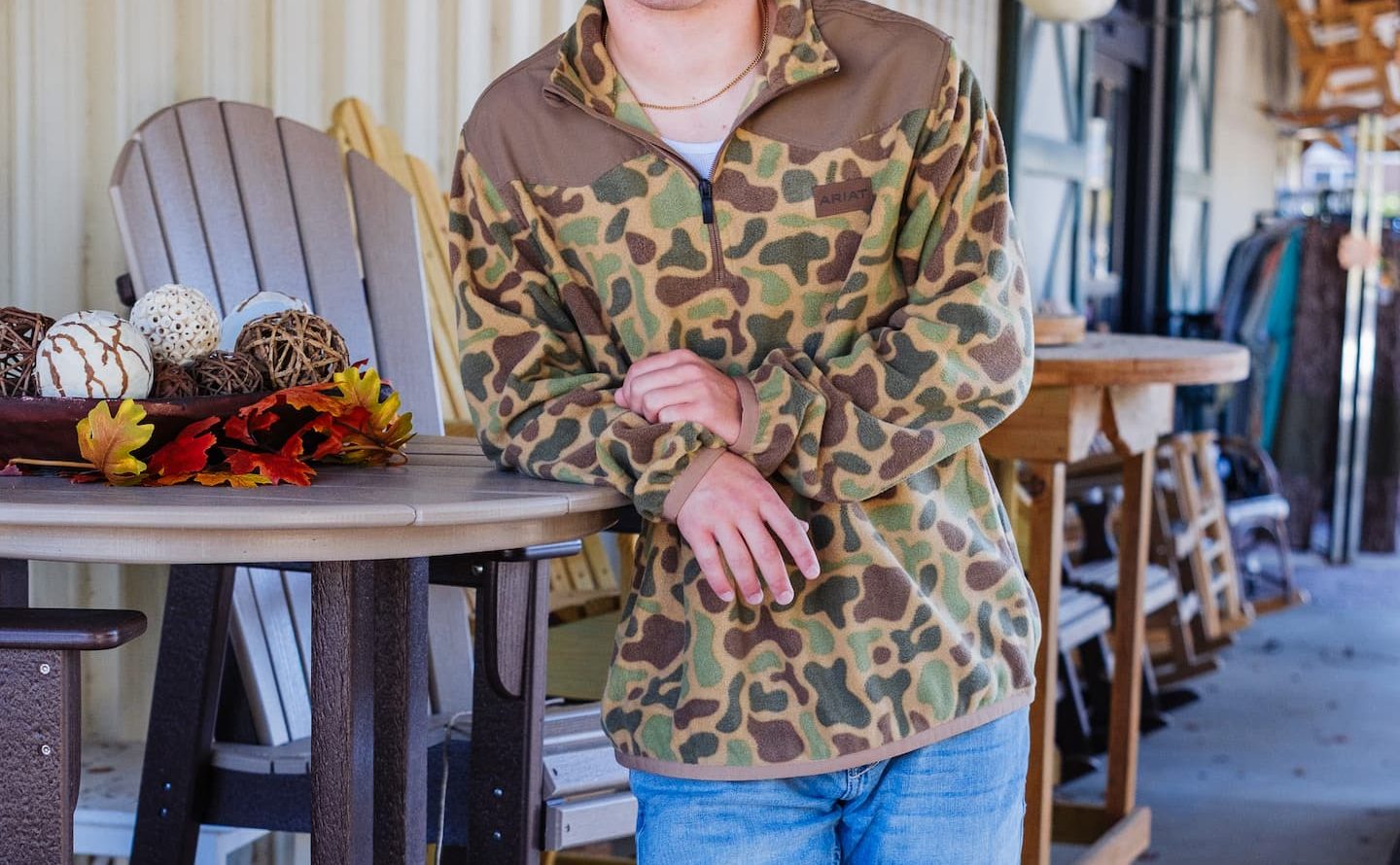 Man wearing Ariat camo pullover, jeans, and leather patch trucker hat from Anderson’s General Store, styled for hunting apparel and outdoor wear in Georgia climates.