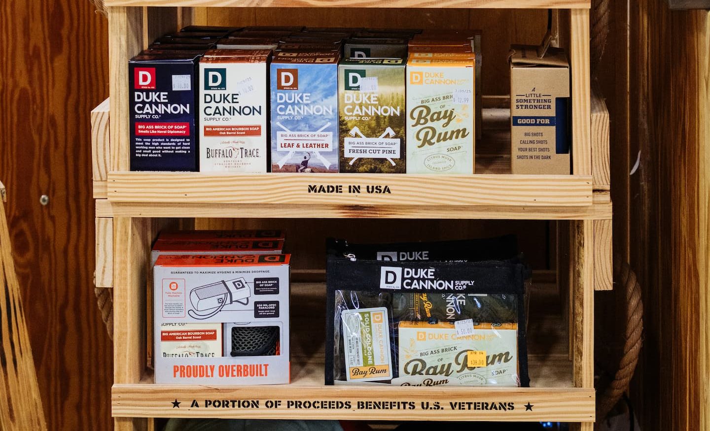 Display shelf at Anderson’s General Store featuring Duke Cannon men’s grooming products, Anderson’s branded hats and tumblers, and YETI camo drinkware, with signage noting proceeds benefit U.S. veterans.